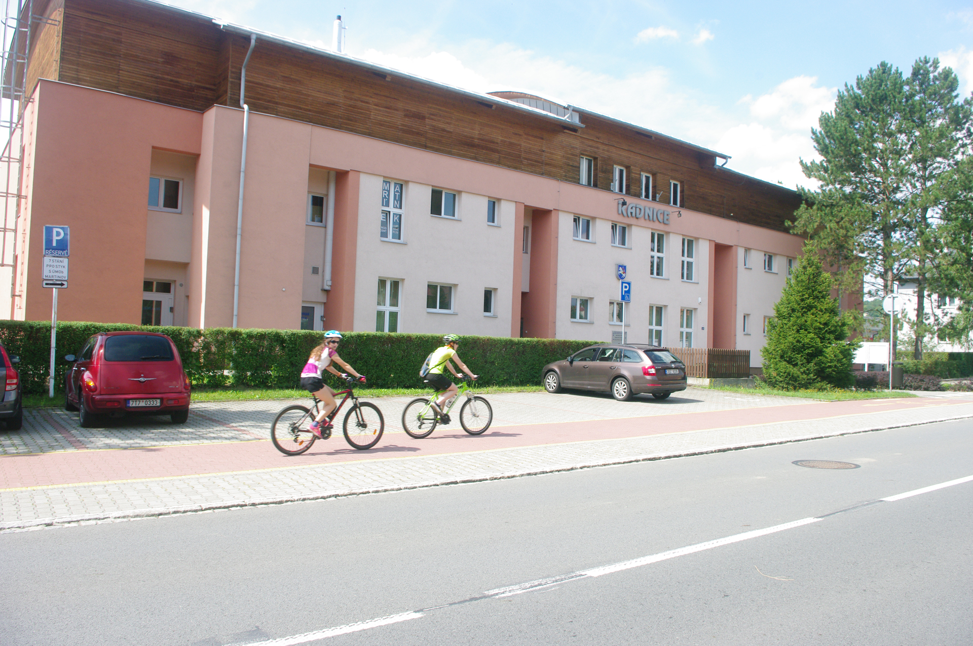 Fotografie radnice v Martinově s projíždějícími cyklisty